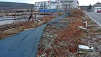 Mrežna ograja in na njej napeto platno je na tleh in razkriva nič kaj mikavno podobo 
nedokončanega gradbišča.