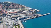 Za javnim parkiriščem je zemljišče ladjedelnice in   za njim nekdanje Delamarisovo dvorišče (vmesne parcele so  v lasti nekdanjih 
Delamarisovih lastnikov). Če bi kdo kupil oboje, bi dobil osem 
hektarjev  veliko območje.    