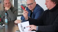 Spomine na bend Deseti brat  so obudili  (z desne) Drago Mislej - Mef, Andrea F. in Vlasti Kozlovič. 
Družno so prelistali novo knjigo,  posvečeno plošči Madona dejmi danes, izdani leta 1985. 