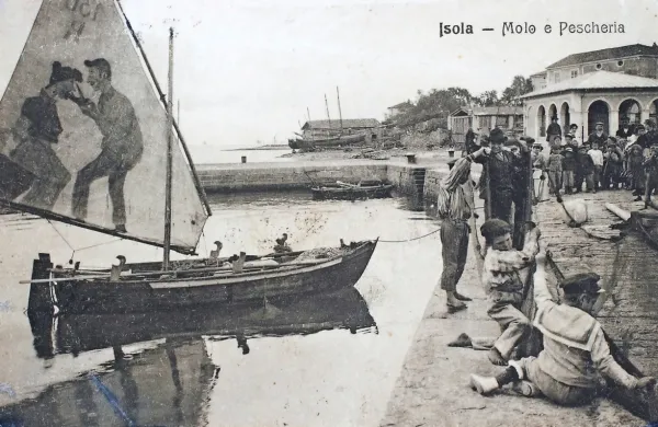 Na največ izolskih razglednicah je   pristanišče, mandrač z Velikim 
trgom ali Porto Apollo. Na jadru ribiške barke  pred  “carinskim 
pomolom”   mož  reže ženi  jezik.   