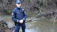 Policist Benjamin Franca ob drevesu, ob katerem so reševali 
47-letno migrantsko mater. 