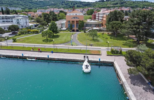 Čeprav je fotografija nastala 19. maja, se od takrat ni veliko 
spremenilo: ob pomolu  E je  namesto  plovil  še vedno videti baraže, 
za njimi pa so še   pivniki in vpojna čreva. V ozadju  je hotel 
Delfin.    