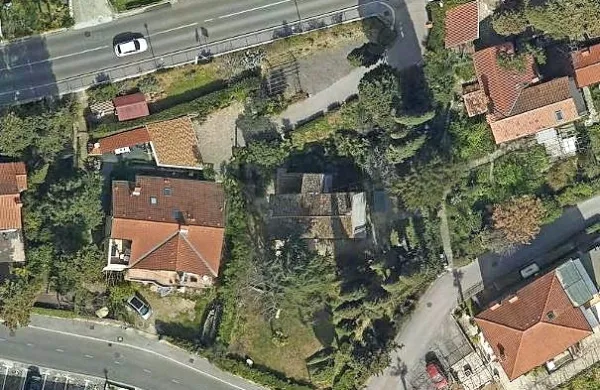 V sredini fotografije je Kosmačeva hiša s temno streho, kot je videti 
iz zraka, okoli nje pa park s stoletnimi drevesi. 