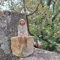  Majhen človeček Urše Toman sedi na skali in opazuje okolico.  