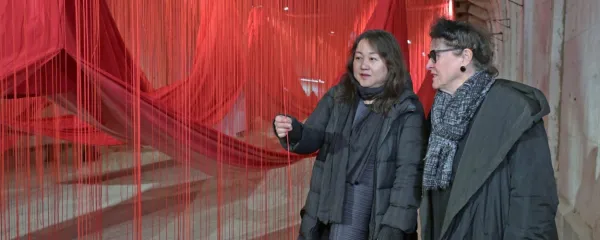 Elisabeth Scweeger, umetniška direktorica Evropske prestolnice 
kulture 2024 v Avstriji in japonska umetnica Chiharu Shiota (z 
desne) pred visečimi rdečimi vrvmi, delom odmevne instalacije v 
predorih nekdanjega koncewntracijskega taborišča Ebensee. 