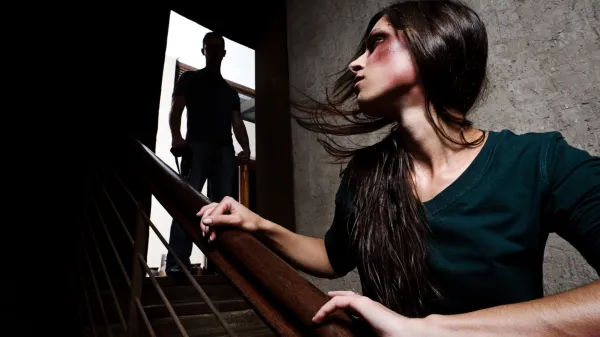 ﻿Concept of domestic abuse. Battered woman escaping from man silhouetted at the top of the stairs, in fear of more violence NASILJE NAD ŽENSKAMI