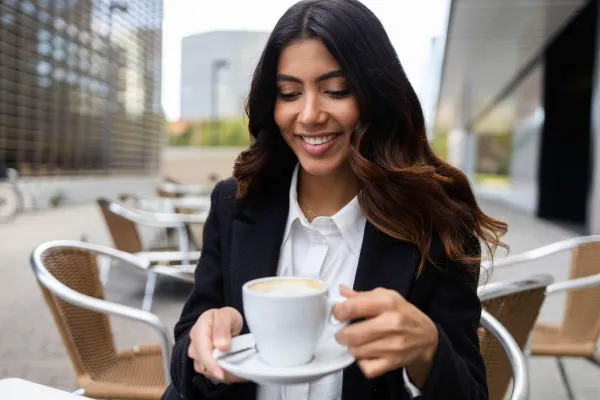 Hispanic Colombian businesswoman enjoying a coffee break at an outdoor cafe. She appears relaxed and smiling, wearing a black blazer and white shirt, with modern buildings behind her.,Image: 1079727404, License: Royalty-free, Restrictions:, Model Release: no, Credit line: Addictive Stock, ADDICTIVE STOCK CREATIVES/Alamy/Profimedia