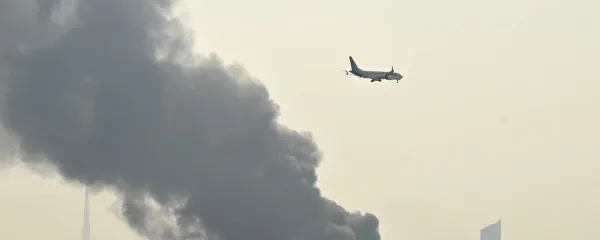 An Emirates aircraft flies past plumes of smoke from an ongoing fire near Dubai International Airport in Dubai on March 16, 2026. Missiles and drone attacks hit across the UAE, with a drone-related incident sparking a fuel tank fire near Dubai airport that disrupted travel, while a missile killed a civilian in Abu Dhabi.,Image: 1083479391, License: Rights-managed, Restrictions: Attention editors: AFP covers the war in the Middle East through its extensive regional network, including bureaus in Tehran, Jerusalem, and several neighboring countries. Since the start of the conflict, journalists have been working under increasingly restrictive conditions. Authorities in several countries have limited reporters' movements, photo and live video coverage from sensitive locations. Some governments and armed groups have banned images of missile or drone strikes and other security-related sites., Model Release: no, Credit line: STR/AFP/Profimedia