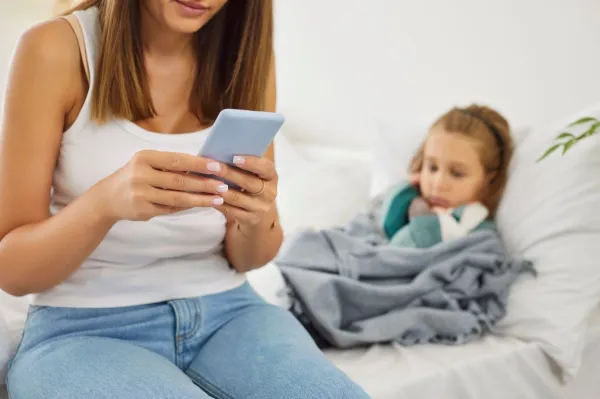 Cropped portrait of young mother calling to pediatrician family doctor for her sick little child lying on bed in bedroom at home suffering from seasonal flu or cold. Medical consultation concept.,Image: 997427608, License: Royalty-free, Restrictions:, Model Release: no, Credit line: Roman Lacheev/Alamy/Profimedia